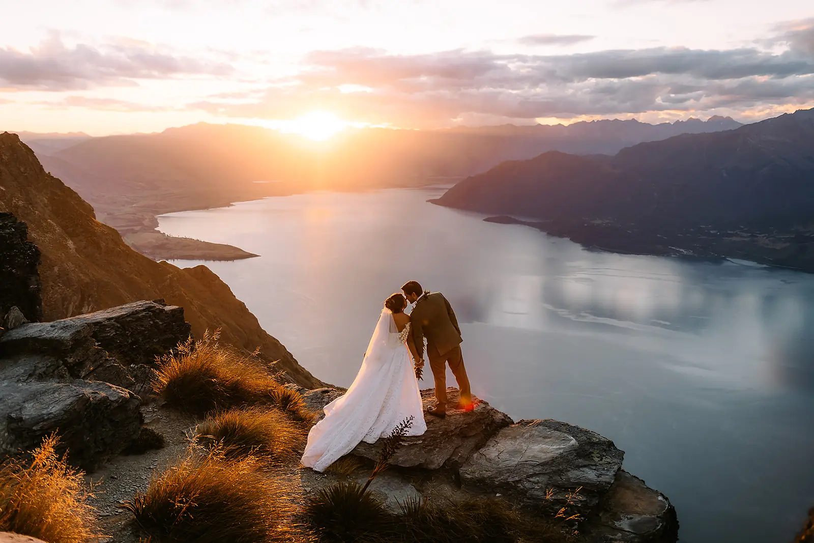 Couple kissing on a clifftop above Lake Wakatipu at sunset during a Queenstown elopement