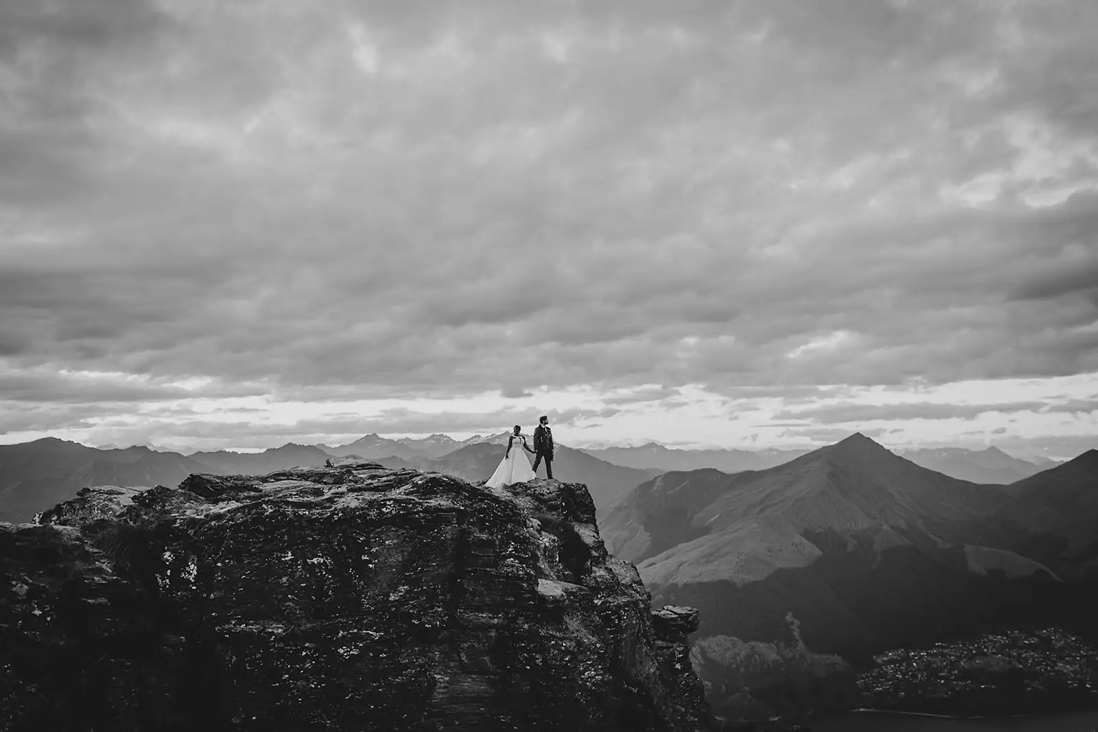 Couple on a cliff edge above Lake Wakatipu under dramatic cloud, in black and white
