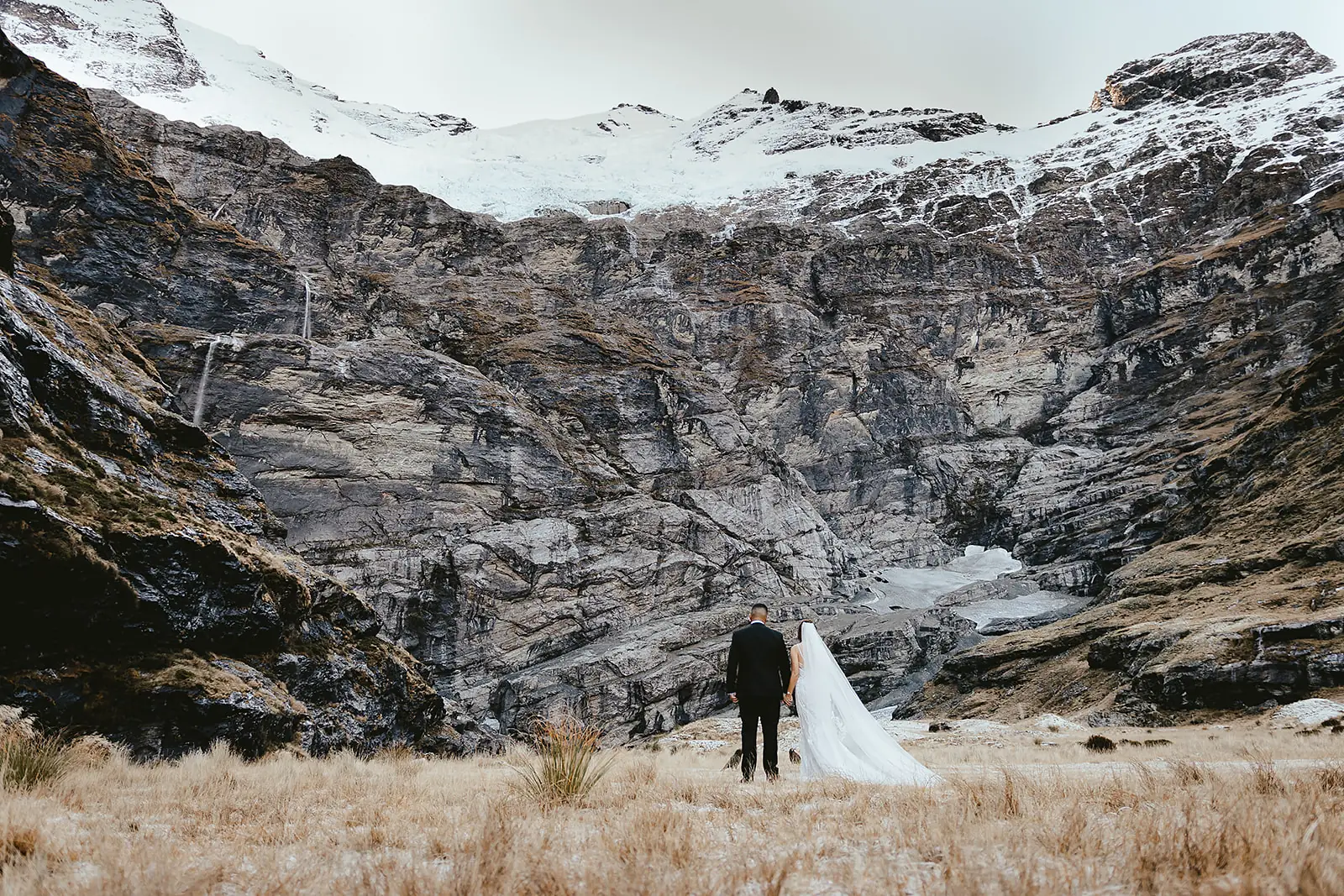 Couple facing the glacier amphitheatre at Earnslaw Burn, the bride's veil lifting in the wind