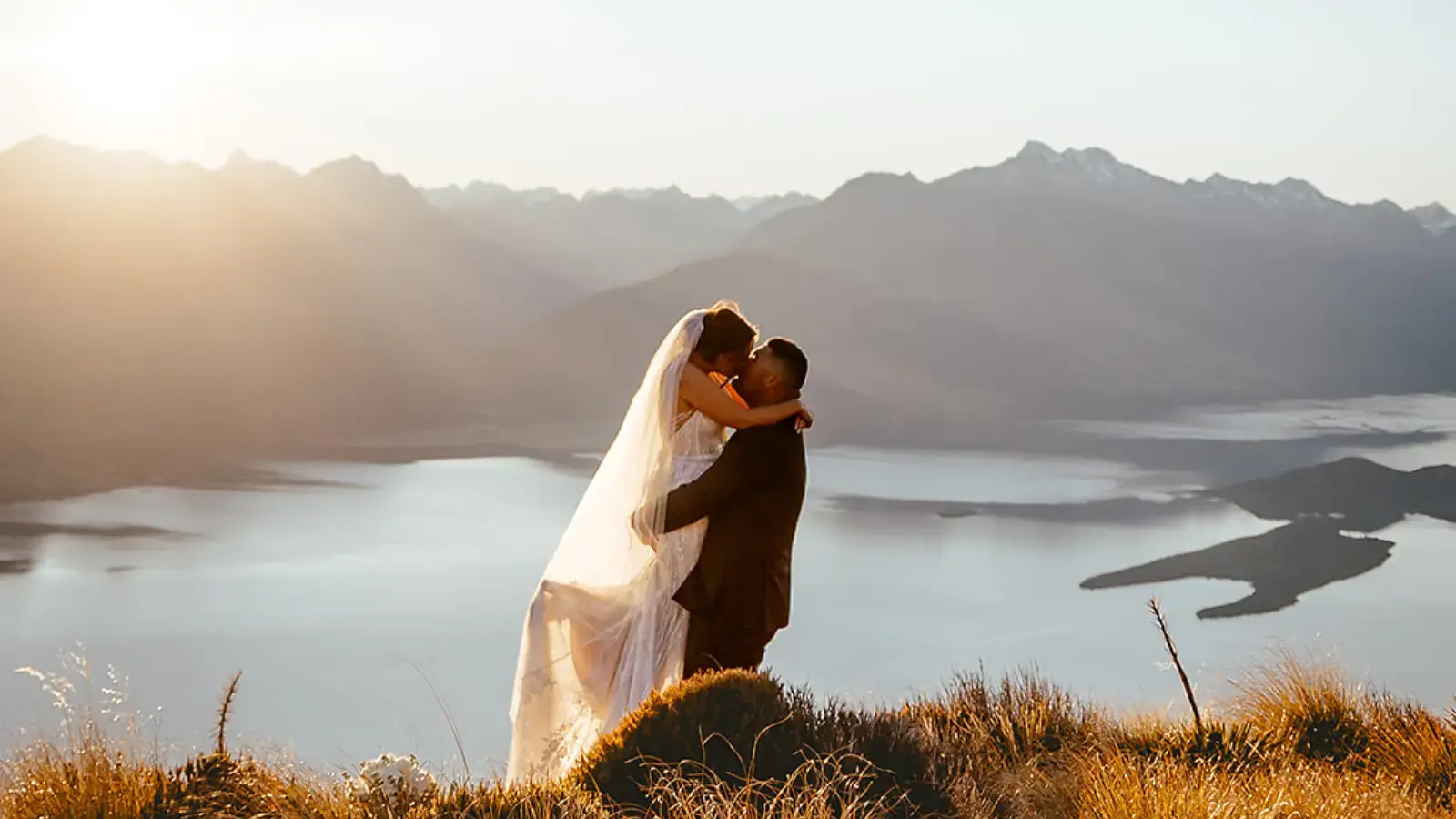 Couple kissing beside a helicopter at sunset on Cecil Peak above Lake Wakatipu