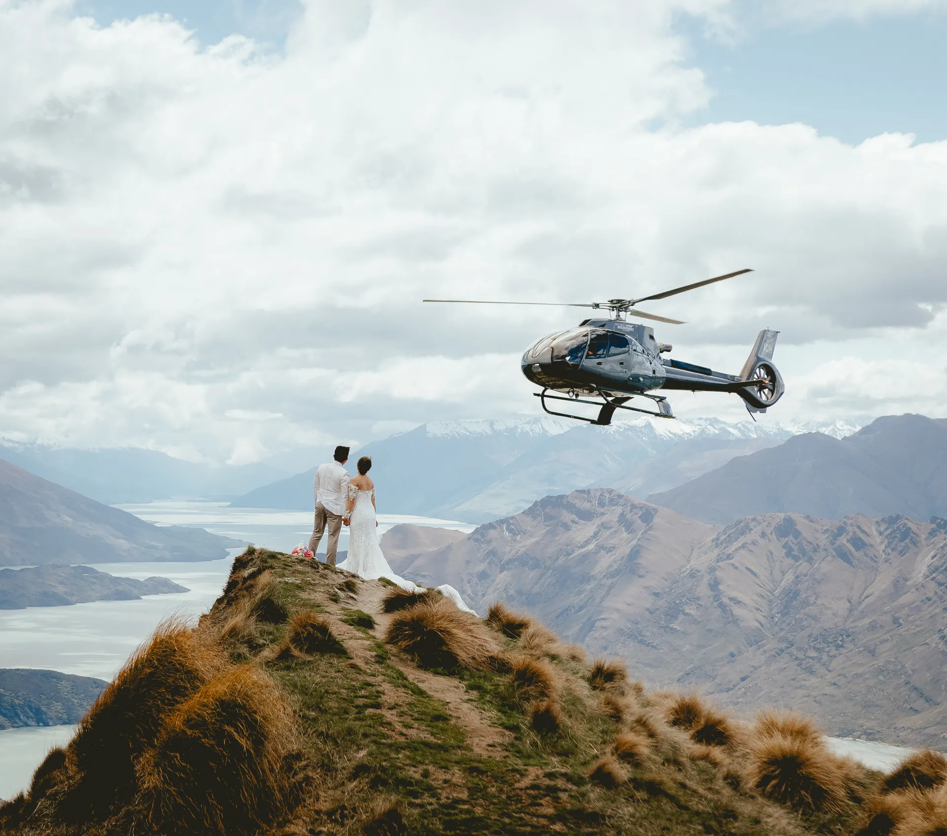 Couple watching a helicopter depart from a mountain ridge after a Queenstown elopement