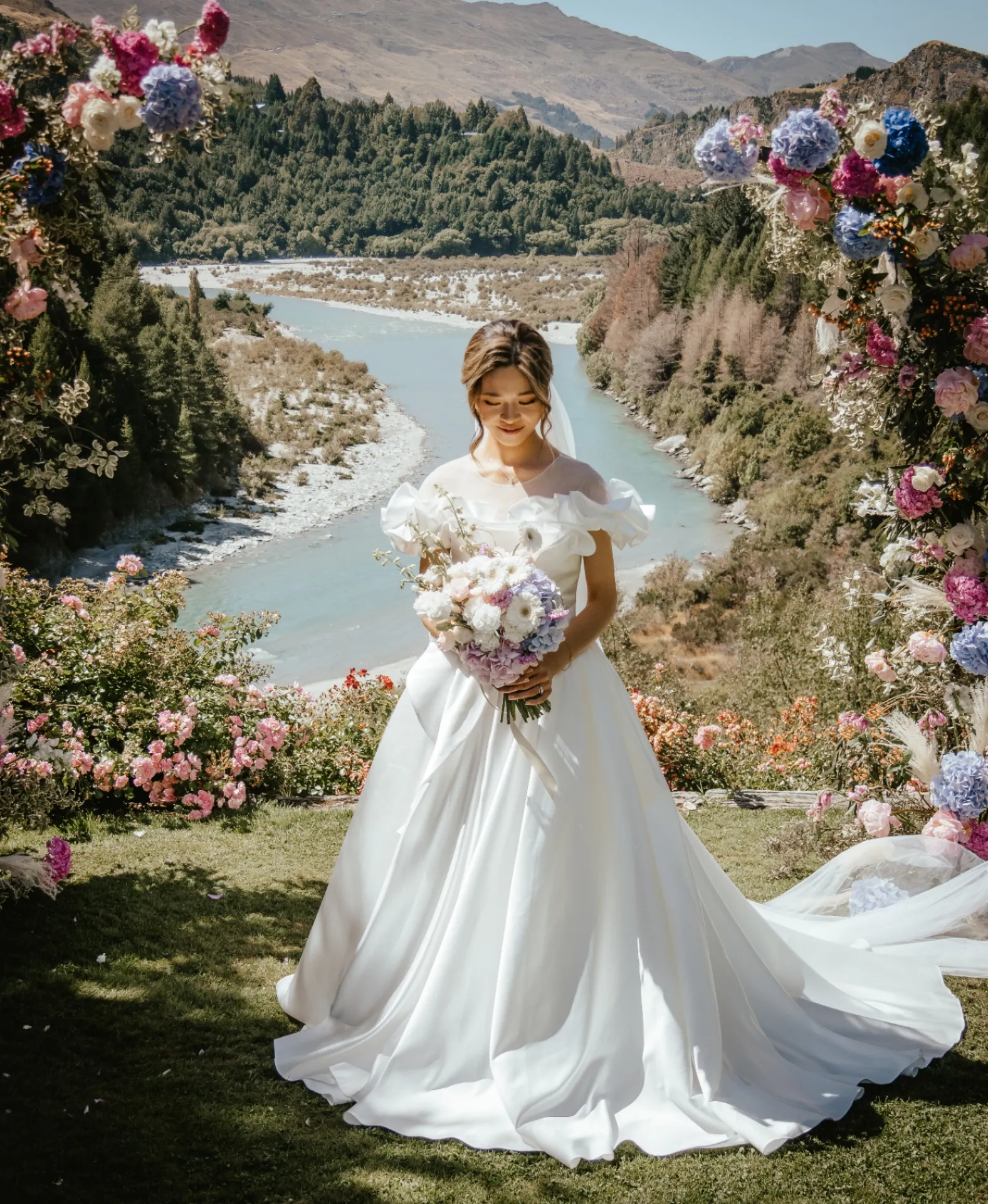 Bride with a bouquet beside a floral arch in an estate garden near Queenstown
