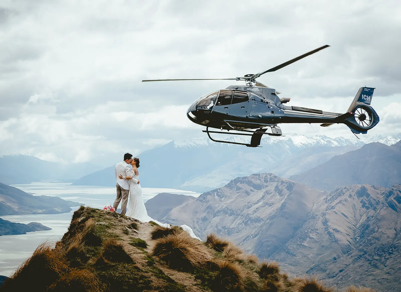 Helicopter passing behind a couple kissing on a snowy Coromandel Peak ridge