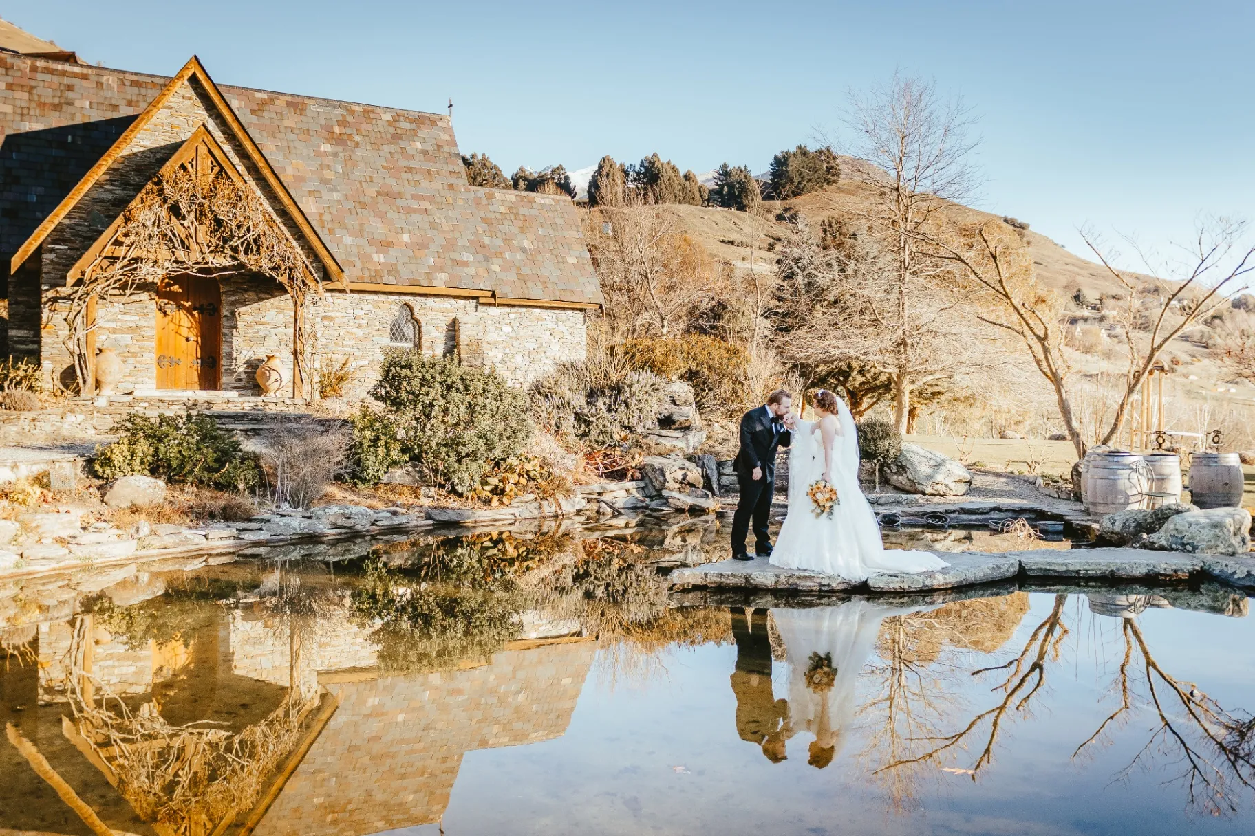 Couple beside a stone chapel reflected in still water near Queenstown