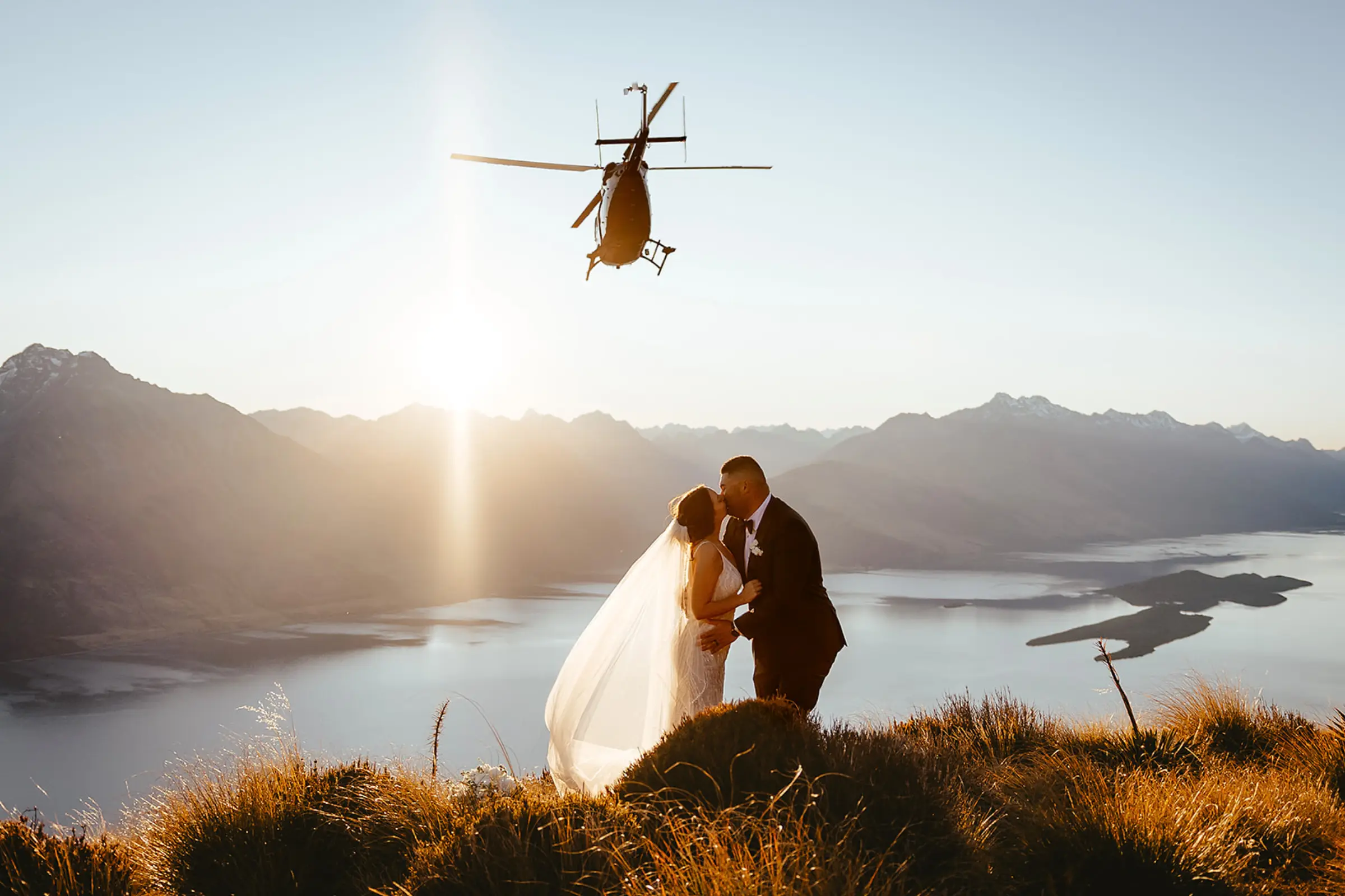 Helicopter passing a couple at sunset above Lake Wakatipu near Mount Crichton