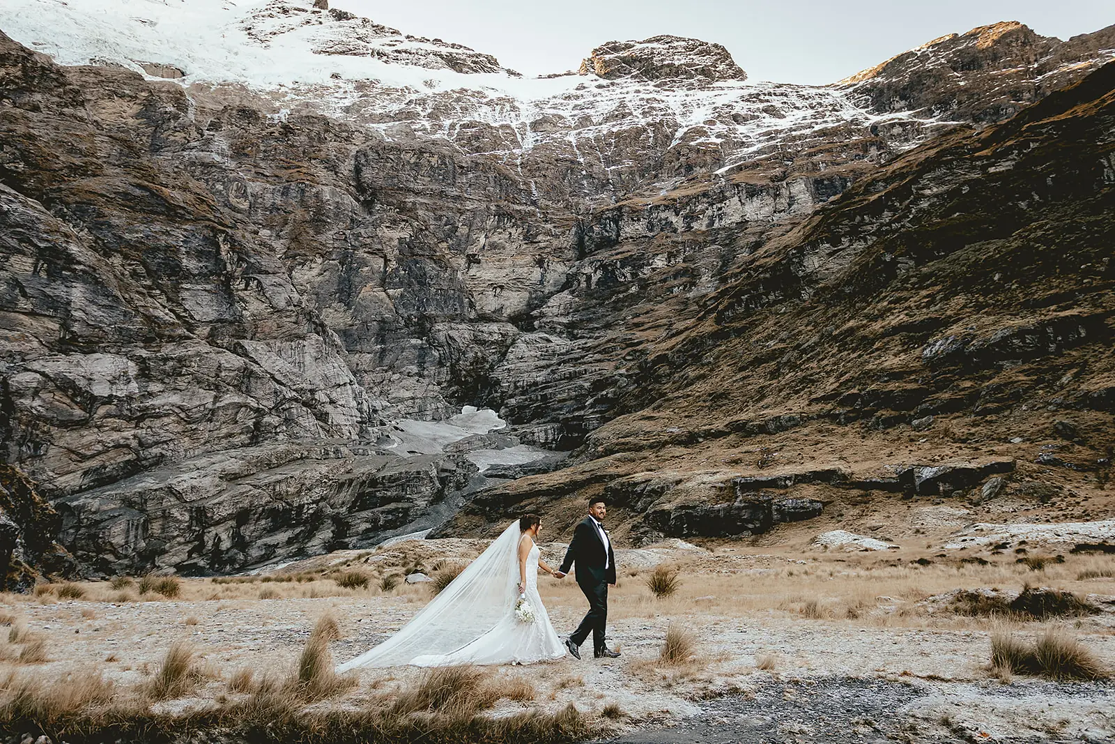 Couple walking across snow beneath the glacier cliffs at Earnslaw Burn
