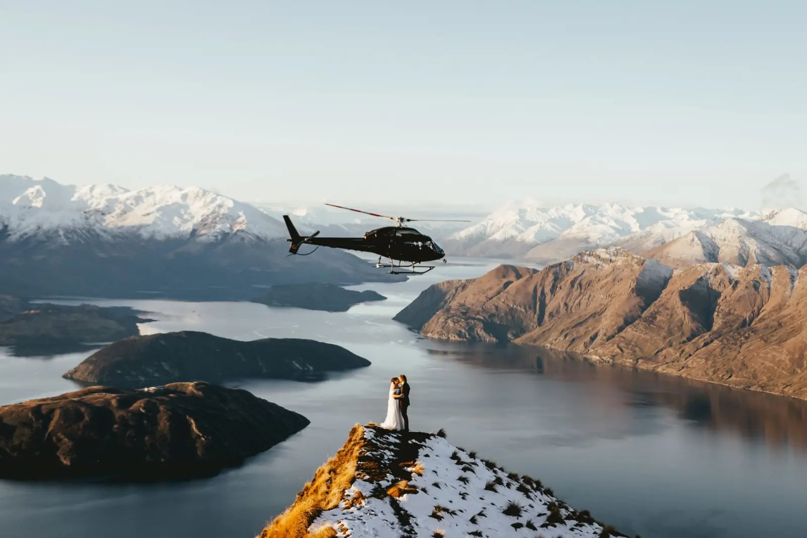 Aerial view of a couple on the Coromandel Peak ridge above Lake Wanaka as a helicopter passes