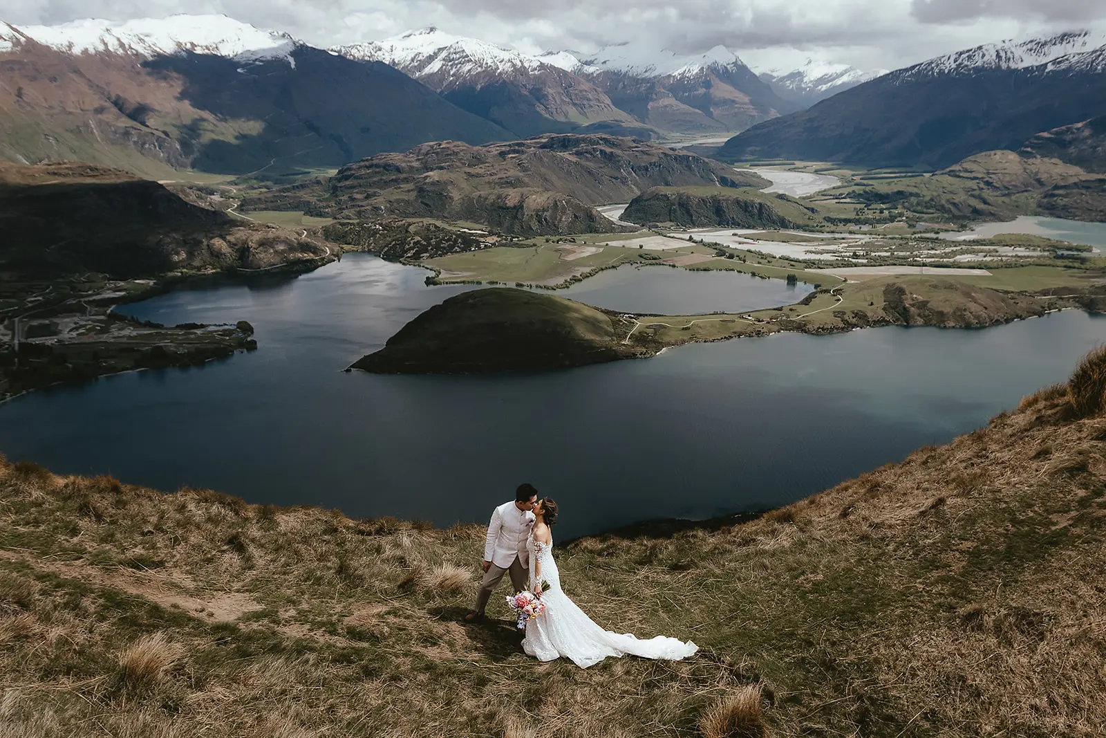 Aerial portrait of a couple kissing above Lake Wanaka with snow mountains behind