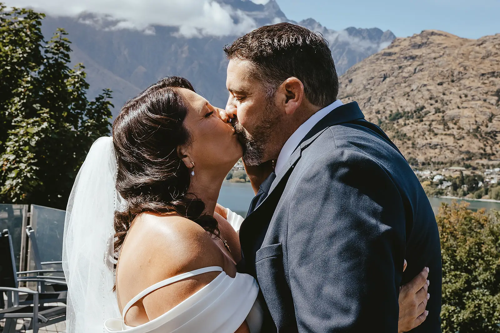 Couple kissing beside Lake Wakatipu with the Remarkables behind them