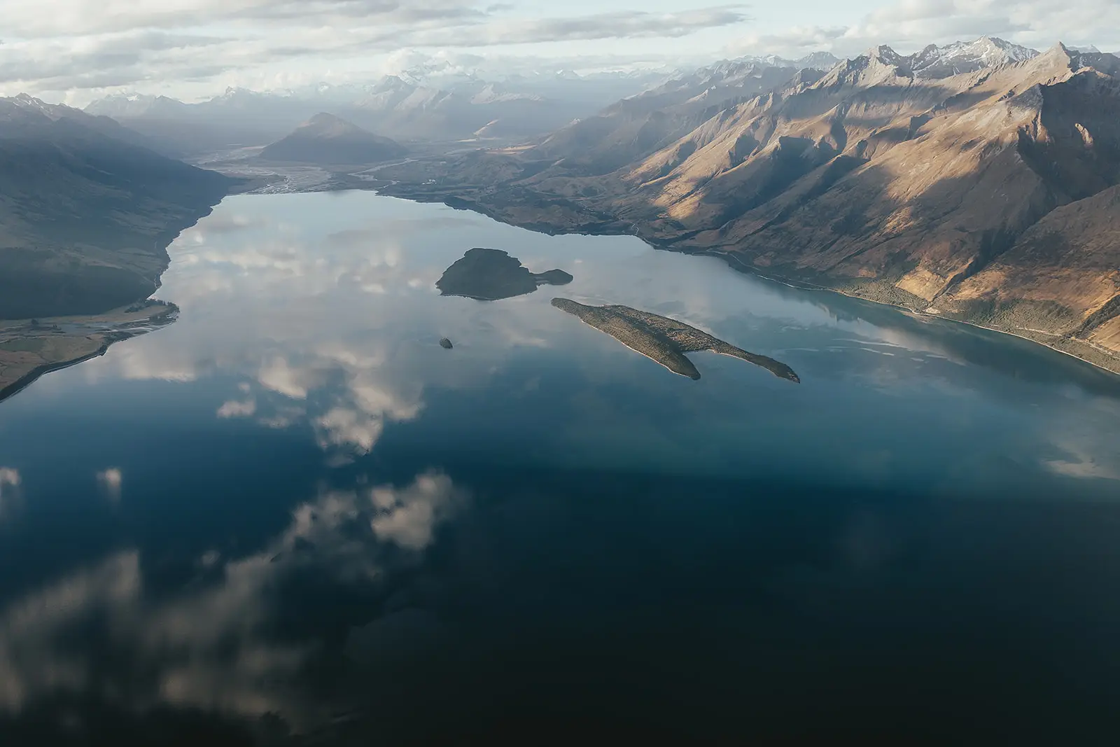 Aerial view of a mirror-calm Lake Wakatipu with islands and mountains reflected