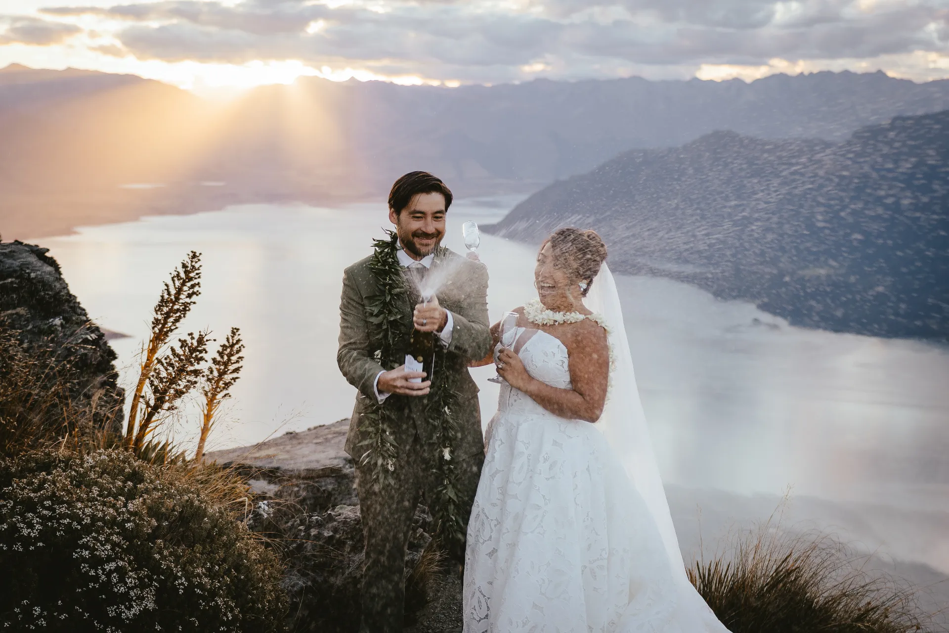 Couple opening champagne on a Queenstown mountaintop in summer light