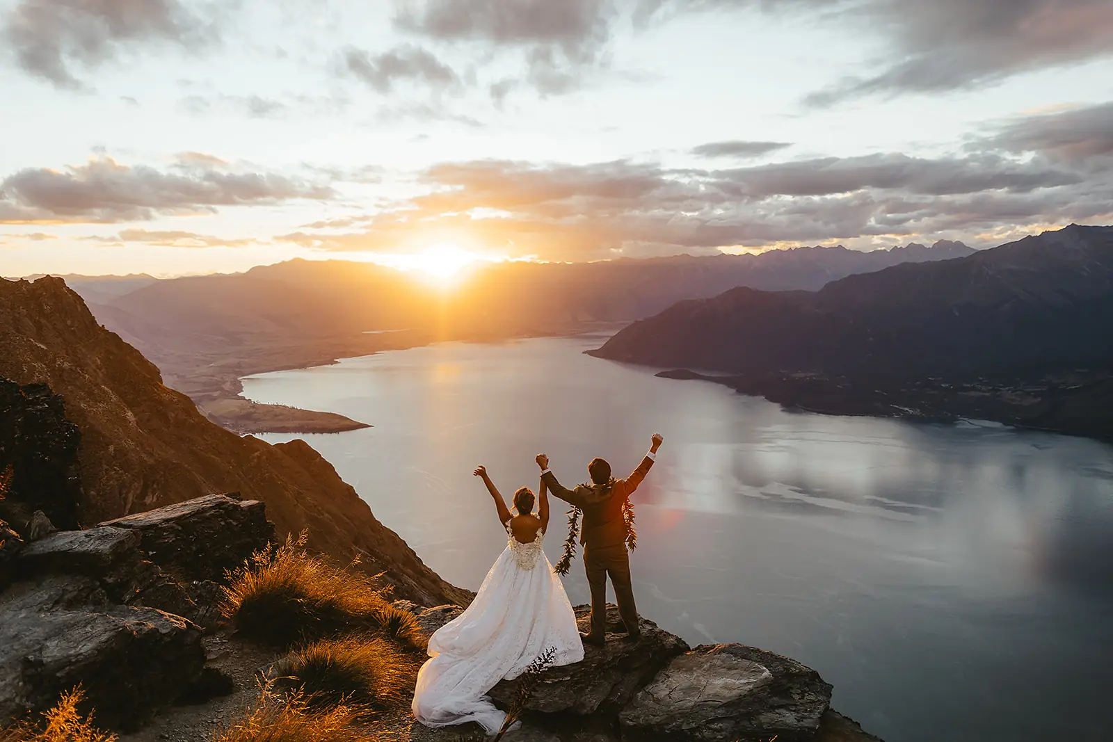 Couple with arms raised at sunset on Cecil Peak above Lake Wakatipu